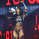 Female performer in blue metallic costume singing into a microphone on stage with red LED screens behind him/her.