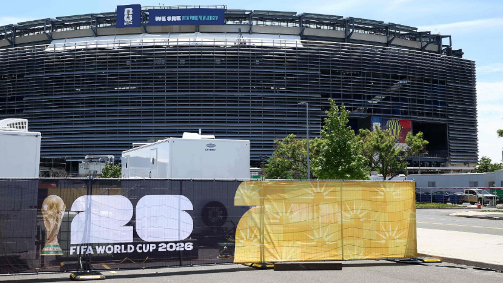 Stadium under construction with a FIFA World Cup 2026 banner and a blue 'We are New York New Jersey' sign on top.