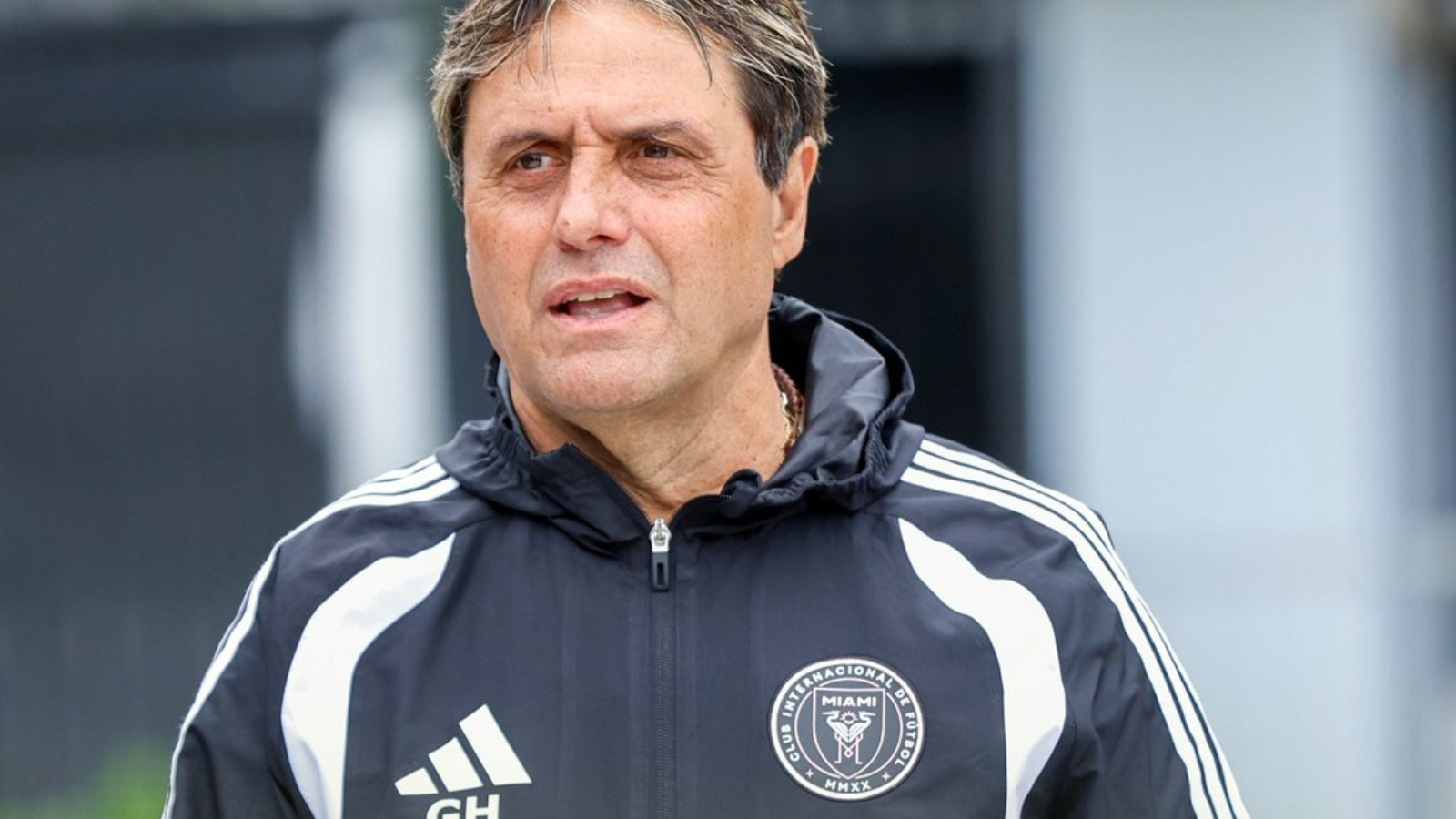 Male coach in a black-and-white training jacket with Miami FC crest, looking to the left outside.