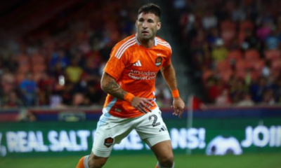 Soccer player in an orange jersey running on a field with a crowd in the background.