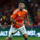 Soccer player in an orange jersey running on a field with a crowd in the background.