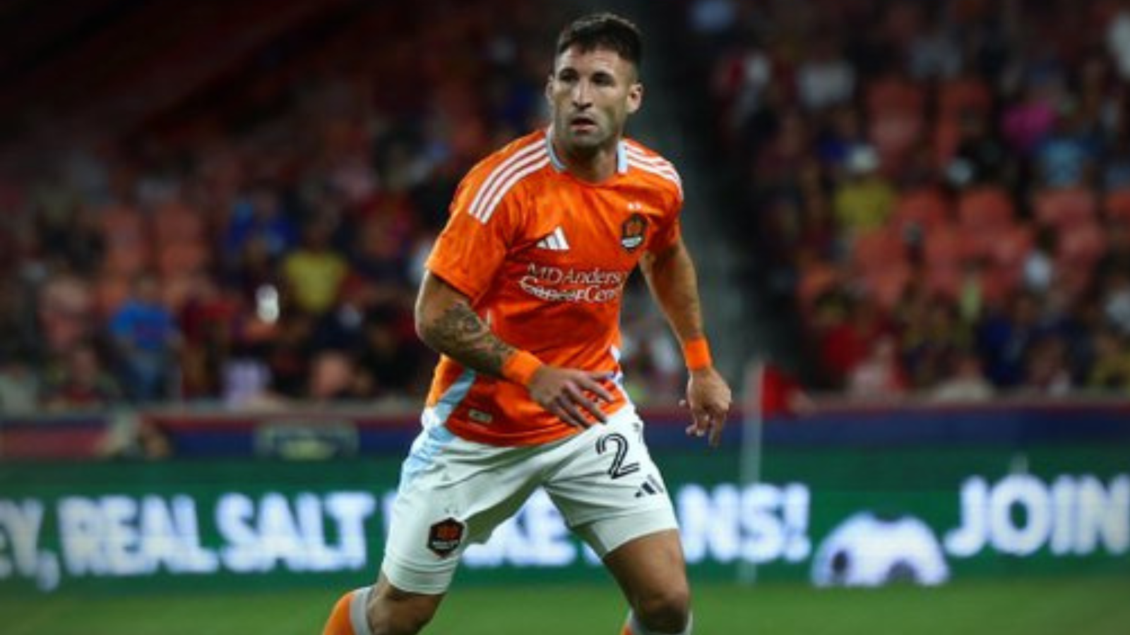 Soccer player in an orange jersey running on a field with a crowd in the background.