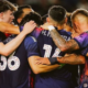 Sports team huddling in a circle, arms around each other, celebrating a win.
