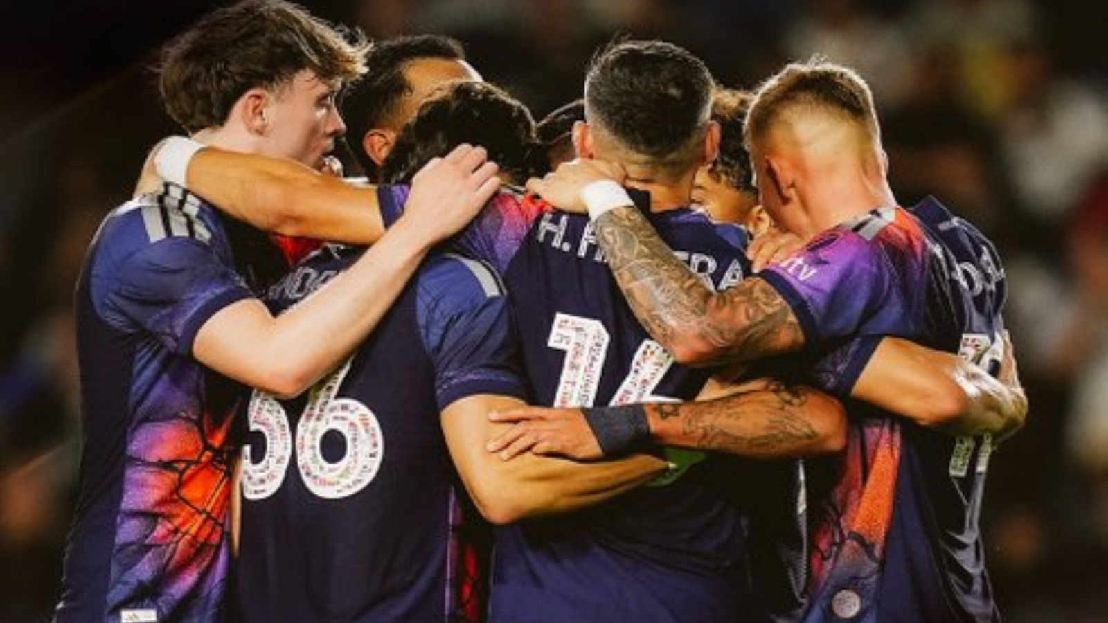 Sports team huddling in a circle, arms around each other, celebrating a win.