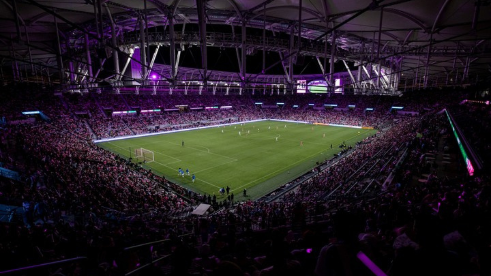 Large soccer stadium at night with players on the field and a packed crowd in the stands?