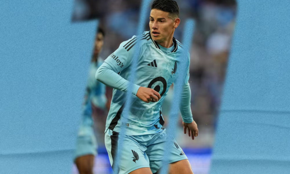 Soccer player in a light blue uniform mid-stride during a match on a blue-toned field background.