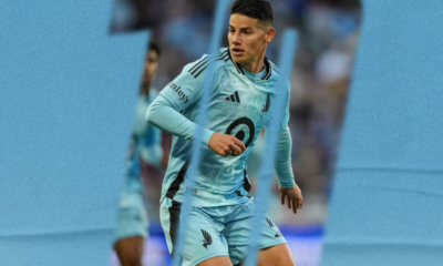 Soccer player in a light blue uniform mid-stride during a match on a blue-toned field background.