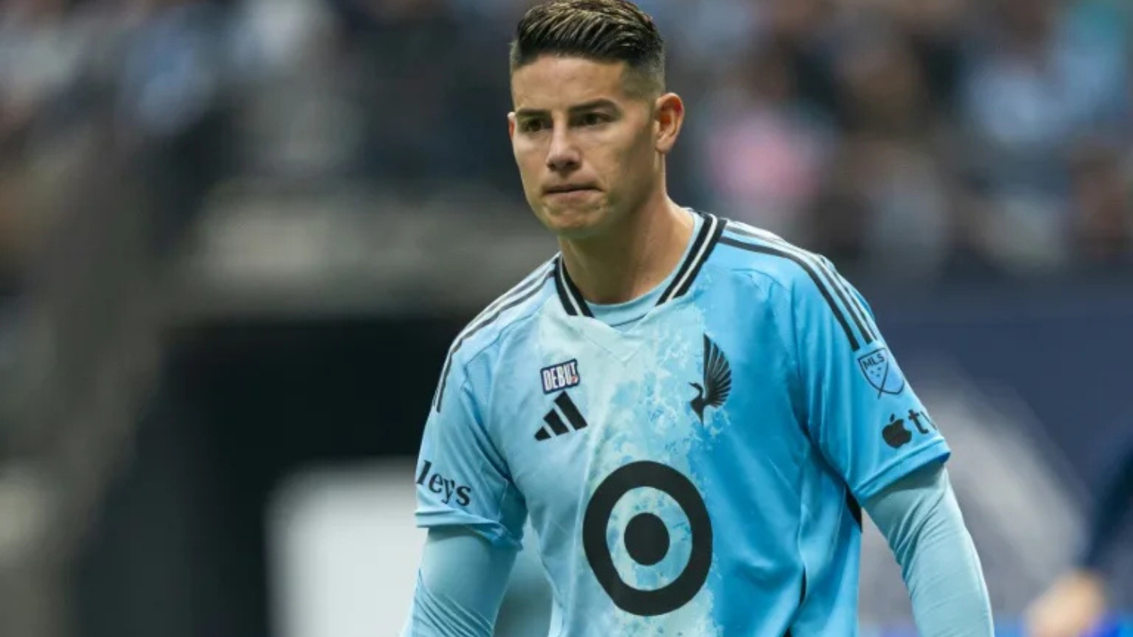 Soccer player in a light blue jersey on the field, looking focused during a match.