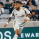 Soccer player in a white LAFC jersey sprinting on the pitch with a cheering crowd in the background.