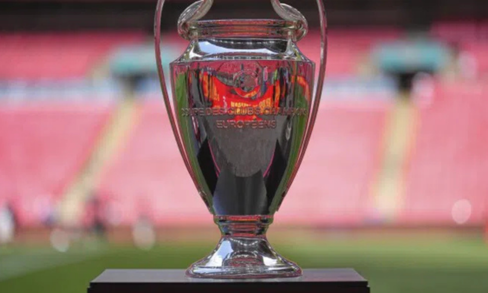 Shiny silver trophy on a black pedestal in a stadium, with blurred pink seating in the background.