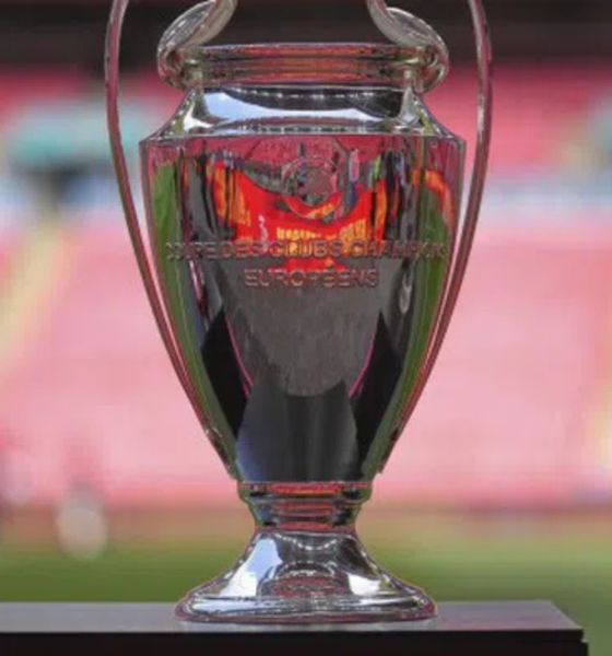 Shiny silver trophy on a black pedestal in a stadium, with blurred pink seating in the background.