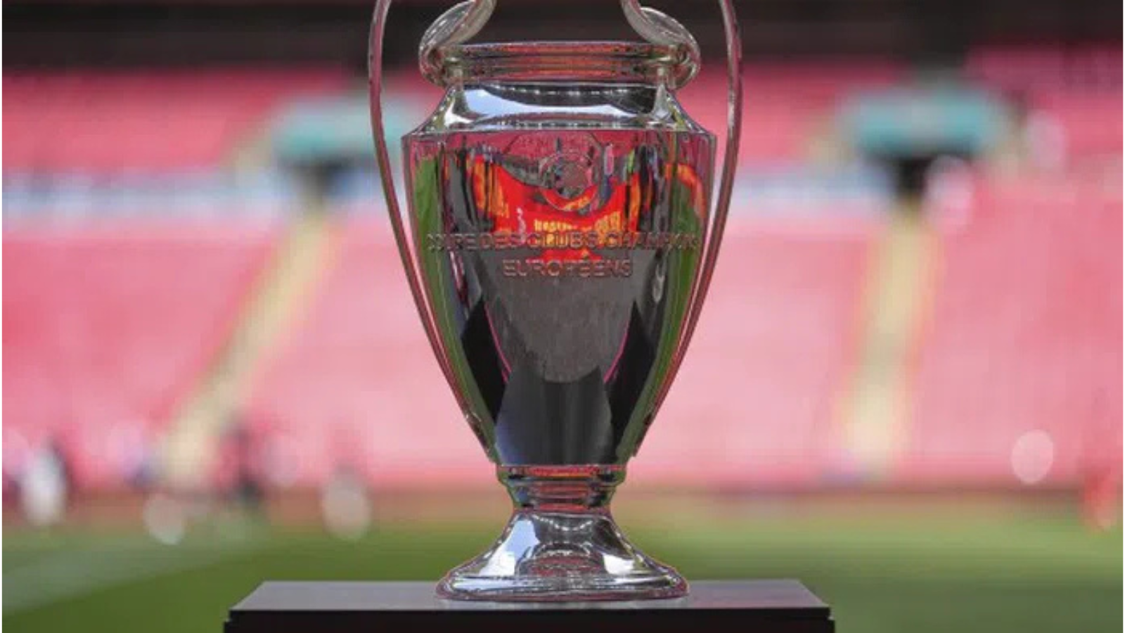 Shiny silver trophy on a black pedestal in a stadium, with blurred pink seating in the background.