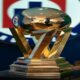 Golden trophy with interlocking angular supports and a reflective spherical top on a tiered pedestal, placed on a dark table in a room with a blurred logo in the background.