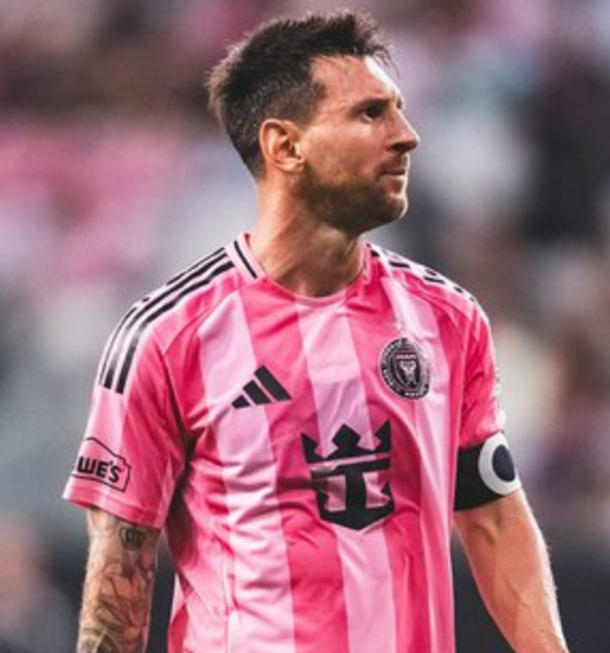 Soccer player in a pink striped jersey with a captain's armband looking to the right on the field.