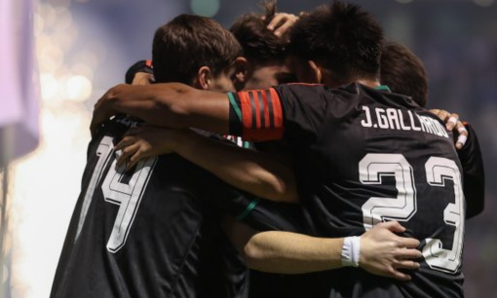 Soccer players in black jerseys hug in a group celebration on the field.