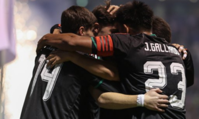Soccer players in black jerseys hug in a group celebration on the field.