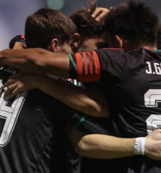 Soccer players in black jerseys hug in a group celebration on the field.