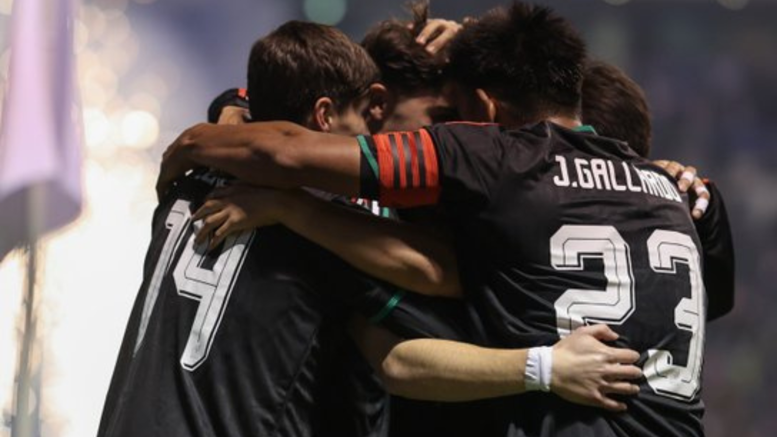 Soccer players in black jerseys hug in a group celebration on the field.