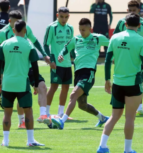 Soccer players in mint green training kits on a grassy field, forming a circle as one player kicks a ball during practice.
