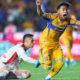 Soccer player in yellow kit jumps in celebration with arms raised, crowd in stadium behind him.