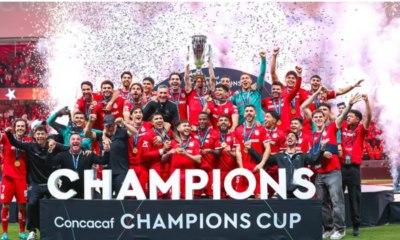 Soccer team in red celebrates winning the CONCACAF Champions Cup, lifting the trophy amid confetti and cheers.