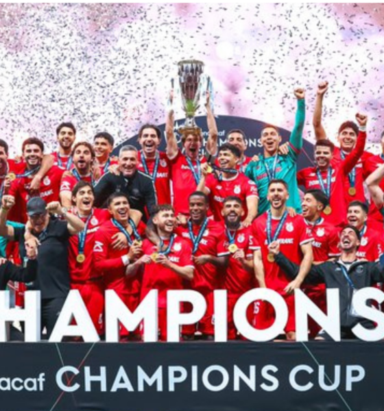 Soccer team in red celebrates winning the CONCACAF Champions Cup, lifting the trophy amid confetti and cheers.