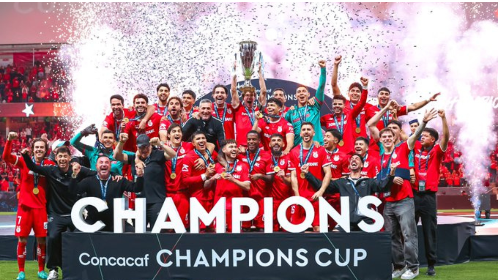Soccer team in red celebrates winning the CONCACAF Champions Cup, lifting the trophy amid confetti and cheers.