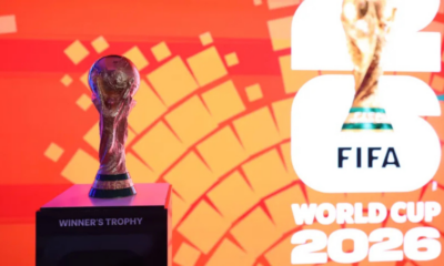 Trophy on a pedestal labeled 'WINNER'S TROPHY' against an orange geometric backdrop, with FIFA World Cup 2026 branding to the right.