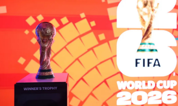 Trophy on a pedestal labeled 'WINNER'S TROPHY' against an orange geometric backdrop, with FIFA World Cup 2026 branding to the right.
