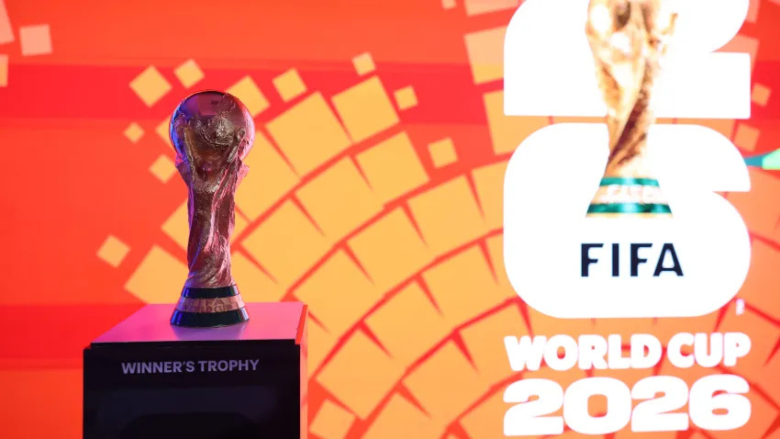 Trophy on a pedestal labeled 'WINNER'S TROPHY' against an orange geometric backdrop, with FIFA World Cup 2026 branding to the right.