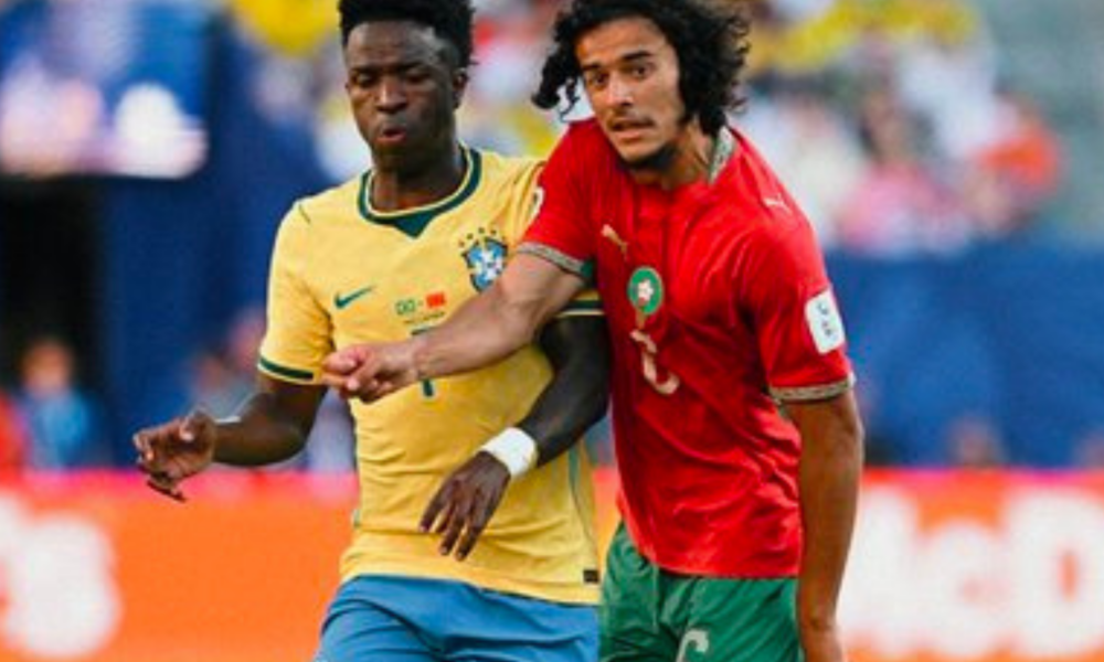 Two footballers compete for the ball during a match, one in a yellow jersey and the other in red and green.