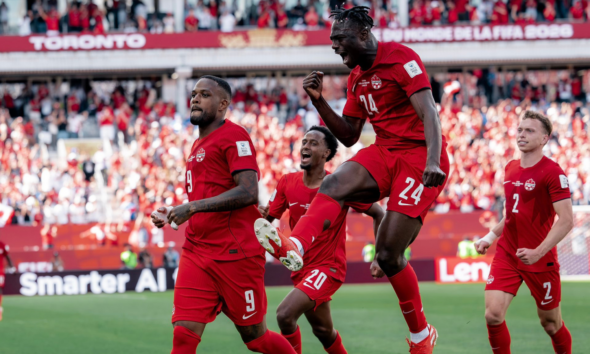 Canadian men's soccer players in red celebrate a goal on the pitch as a full stadium cheers.