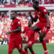 Canadian men's soccer players in red celebrate a goal on the pitch as a full stadium cheers.