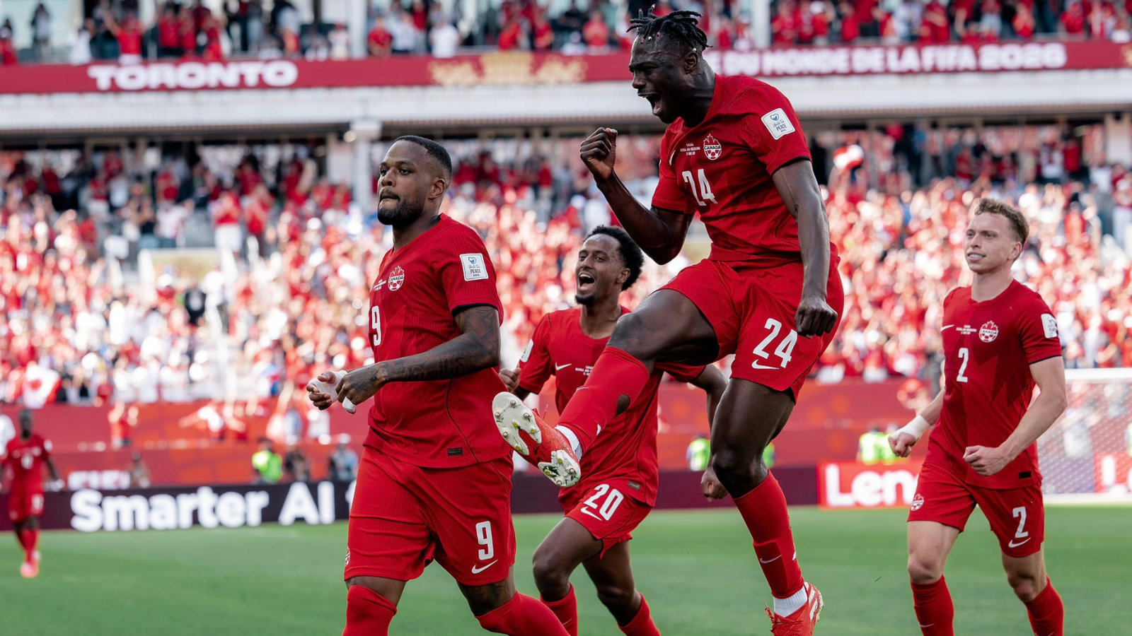 Canadian men's soccer players in red celebrate a goal on the pitch as a full stadium cheers.