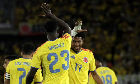 Colombian soccer players celebrate on the field, high-fiving in yellow jerseys; Sanchez #23 and Diaz #7 visible on their backs.