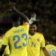 Colombian soccer players celebrate on the field, high-fiving in yellow jerseys; Sanchez #23 and Diaz #7 visible on their backs.