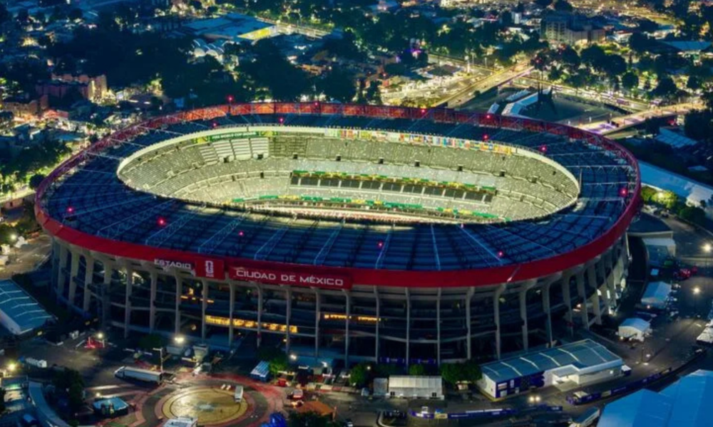 Aerial night view of a large circular stadium with a red outer ring and bright green field, Ciudad de México signage visible on the stands.