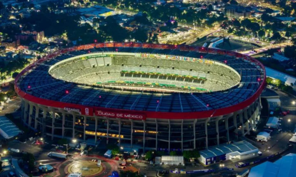 Aerial night view of a large circular stadium with a red outer ring and bright green field, Ciudad de México signage visible on the stands.