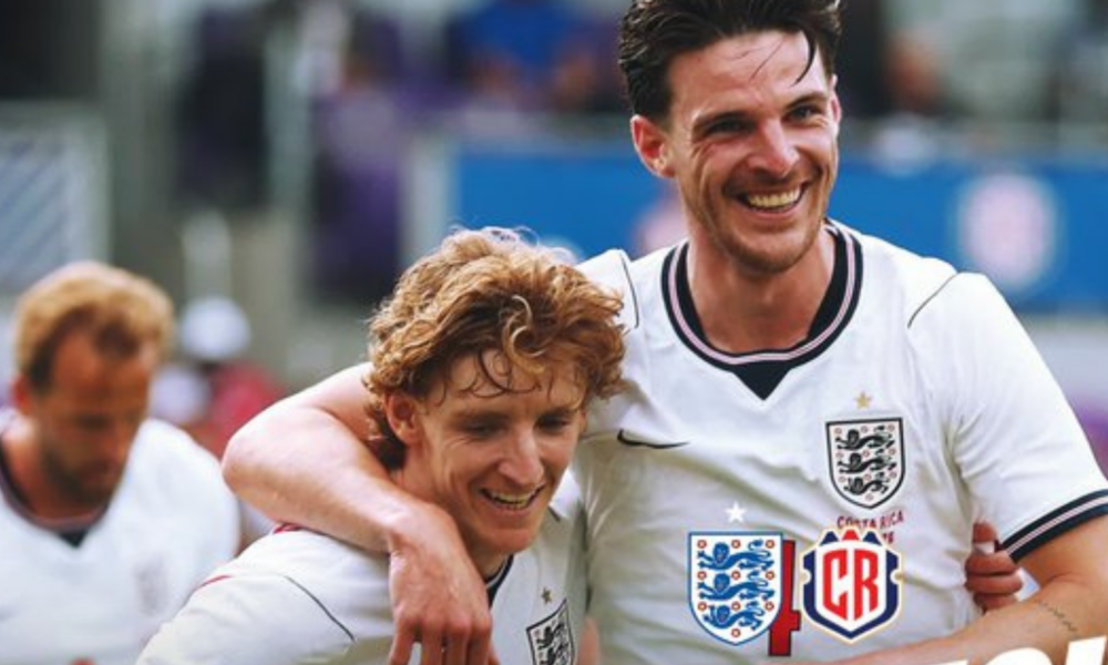 Two England footballers celebrate, arms around each other, smiling on the pitch after a game.