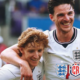 Two England footballers celebrate, arms around each other, smiling on the pitch after a game.