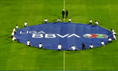 A large blue banner reading 'LIGA BBVA' laid out on a green soccer field with people around it