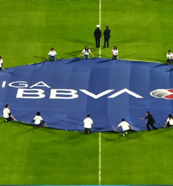 A large blue banner reading 'LIGA BBVA' laid out on a green soccer field with people around it