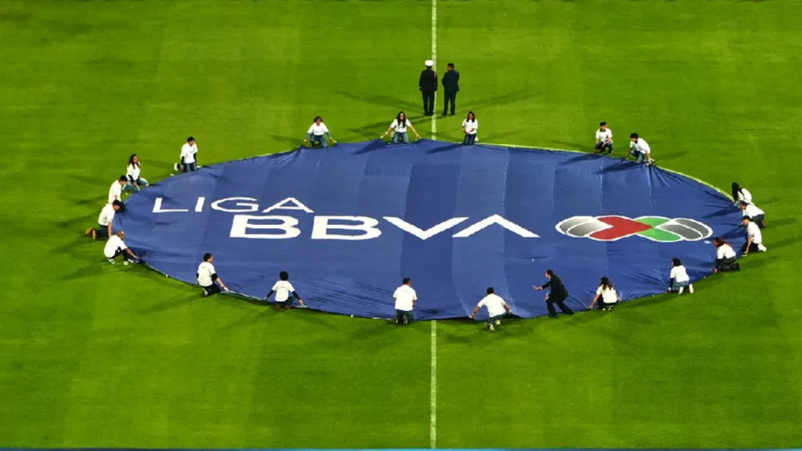 A large blue banner reading 'LIGA BBVA' laid out on a green soccer field with people around it