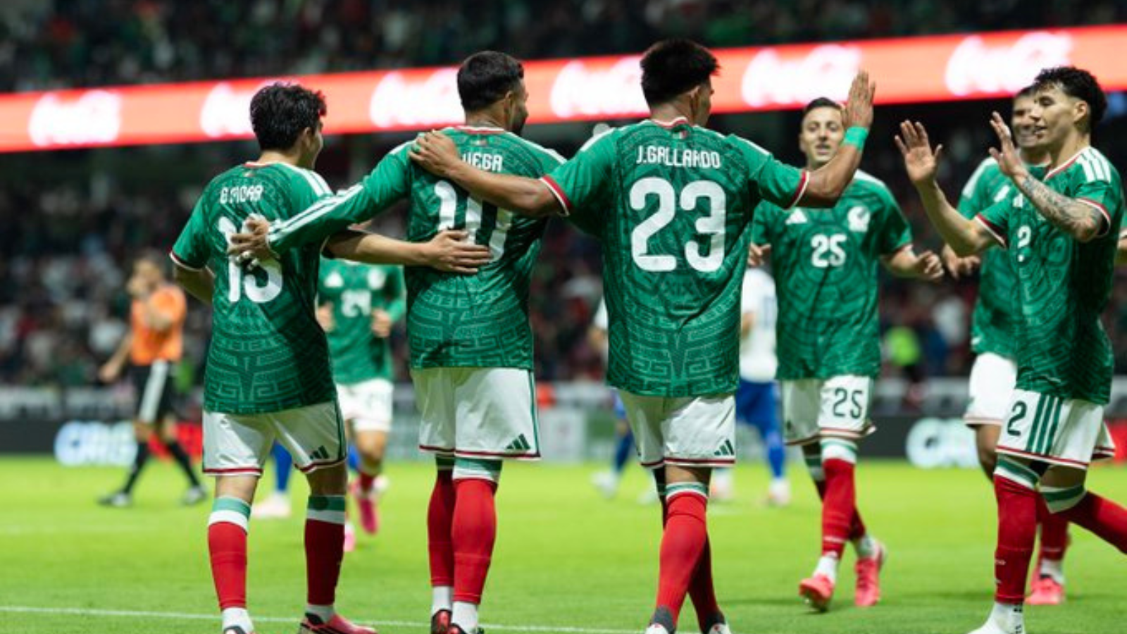Soccer players in green jerseys celebrate with arms around each other on the field.