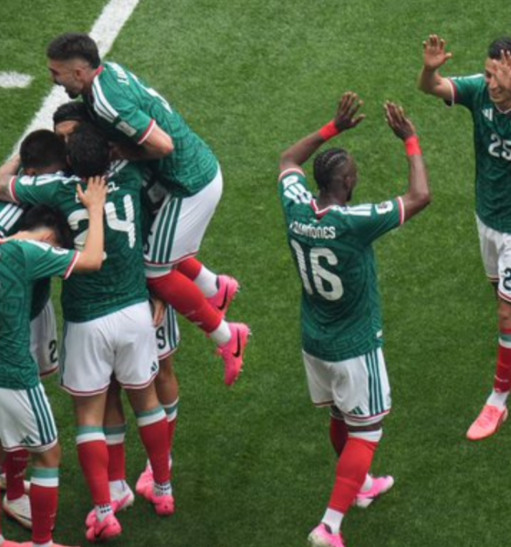Group of soccer players in green jerseys celebrate together on a grass pitch, embracing and jumping in celebration after a goal