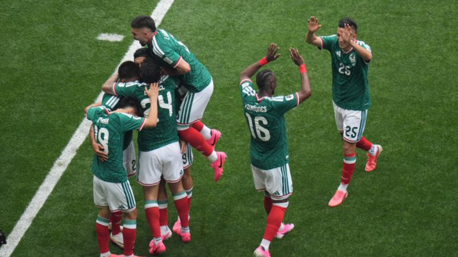 Group of soccer players in green jerseys celebrate together on a grass pitch, embracing and jumping in celebration after a goal