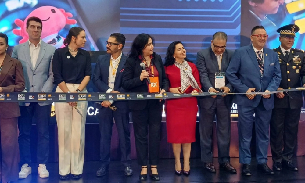 Group of professionals in formal attire cutting a ribbon at a ceremony on a stage with a blue backdrop.