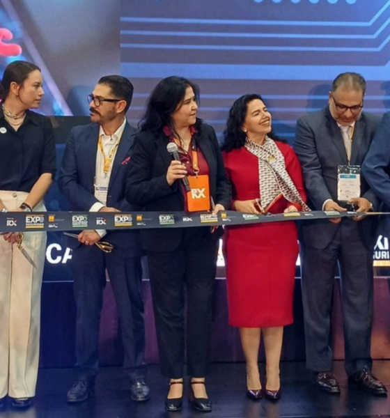 Group of professionals in formal attire cutting a ribbon at a ceremony on a stage with a blue backdrop.