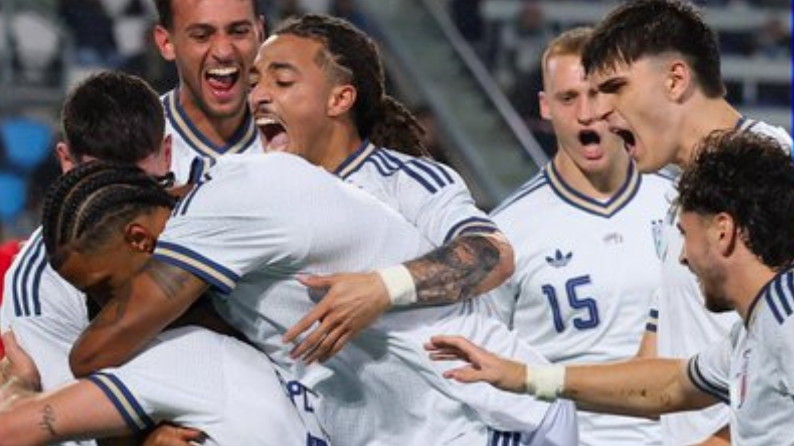 Soccer players in white uniforms celebrate with a group hug on the field, arms around each other in joy.