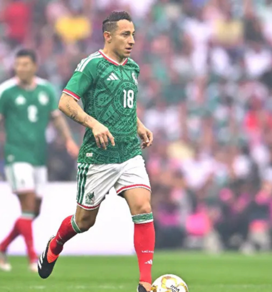 Soccer player in a green Mexico jersey (number 18) dribbling the ball on a green field with a blurred stadium crowd in the background.